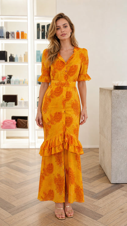 Front full view of woman wearing Marigold yellow paisley belted maxi dress with tiered ruffle skirt