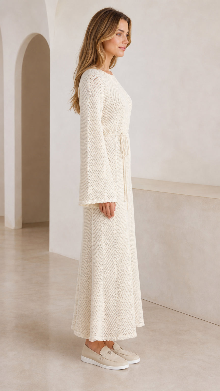 Side profile of model in cream long knit maxi dress with bell sleeves
