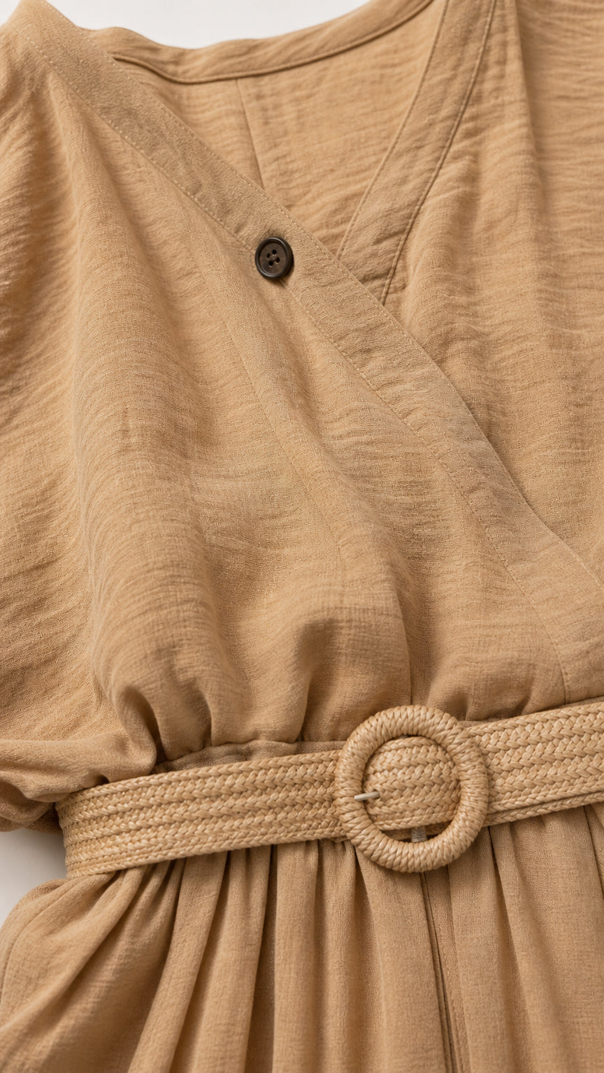 Close-up detail of beige crinkle fabric, crossover button, and woven belt buckle