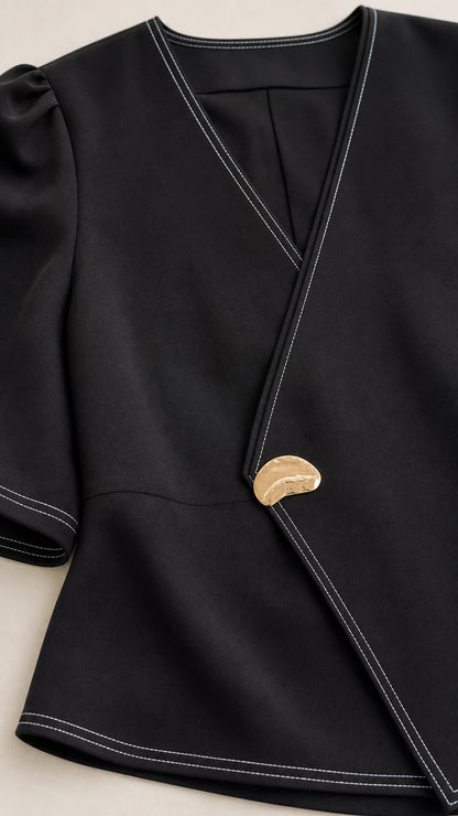 Close-up detail of black top neckline, white contrast topstitching, and gold sculptural button closure