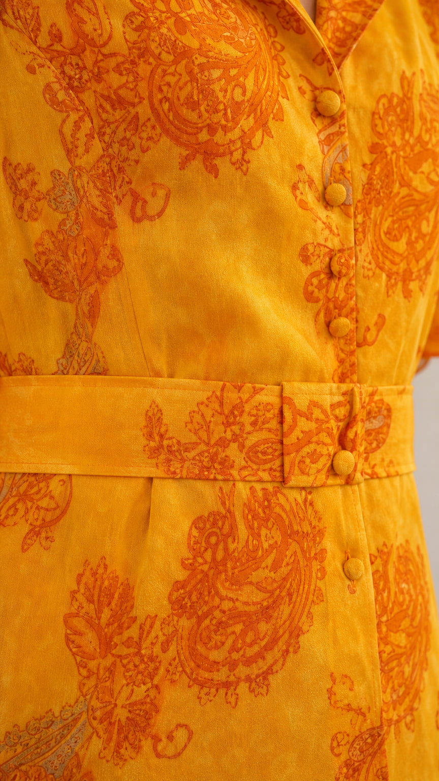 Close-up detail of paisley fabric pattern, covered buttons, and fabric belt buckle