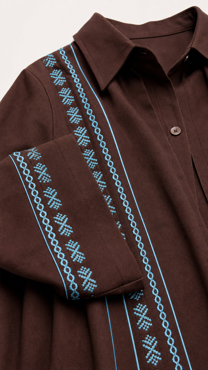 Close-up detail of point collar and cyan geometric embroidery on brown fabric placket and cuff