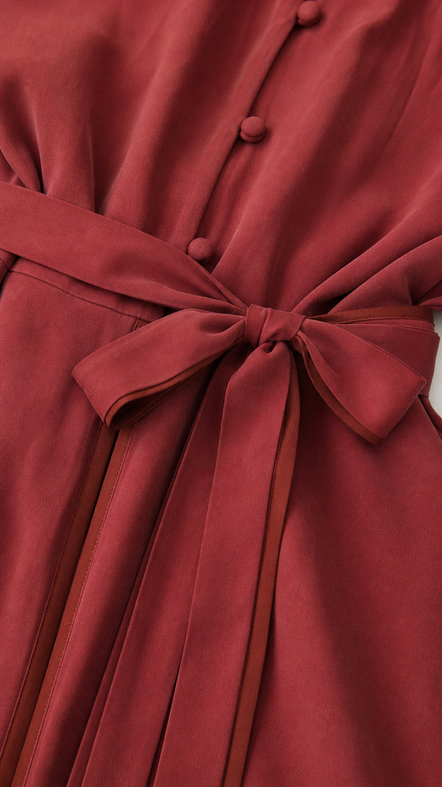 Close-up detail of covered buttons and self-tie bow sash on rust red maxi dress