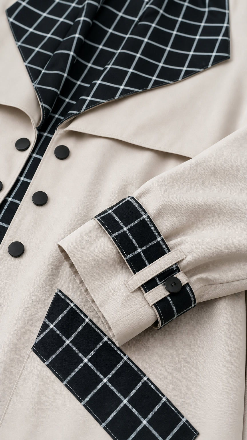 Close-up detail of beige trench coat fabric, buttons, grid lapel, cuff tab, and pocket border